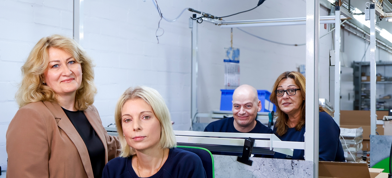 Vier Personen in einem technischen Arbeitsumfeld mit Monitoren und Kabeln im Hintergrund