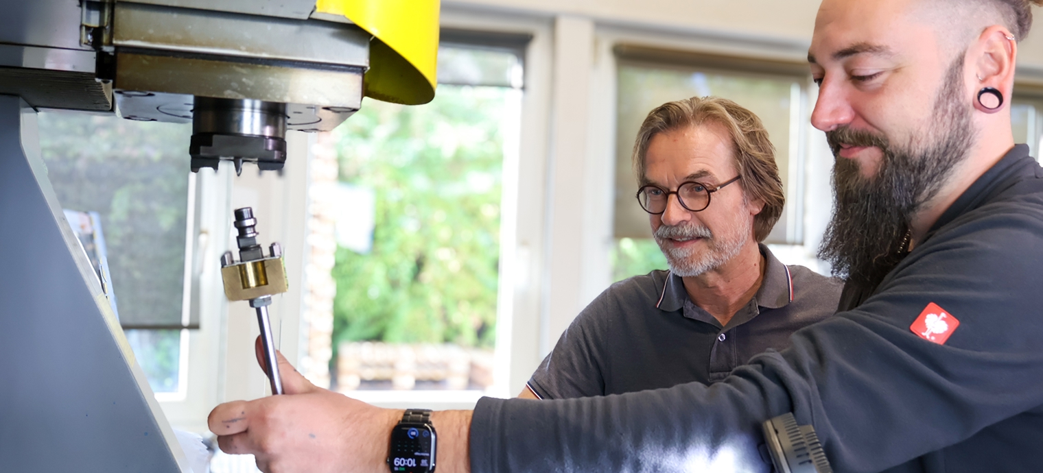Zwei Männer stehen an einer Werkzeugmaschine, einer hält ein Werkzeugteil in der Hand