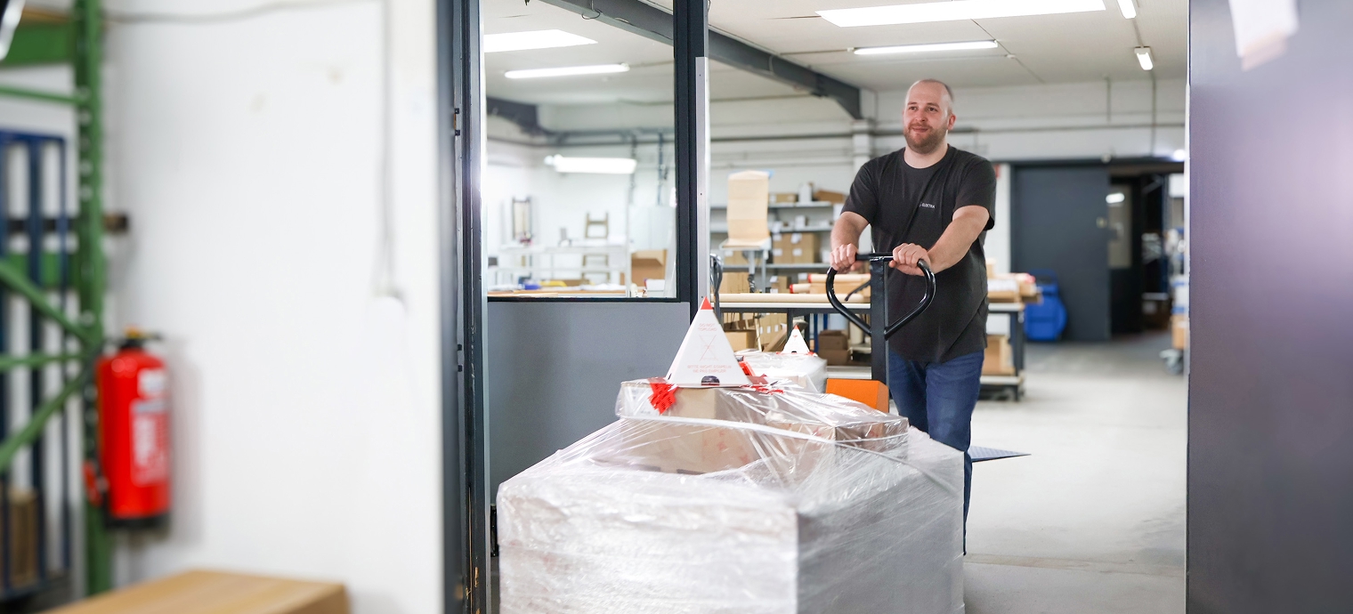 Person schiebt in einer Lagerhalle einen mit Folie verpackten Palettenwagen